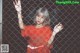 A woman in a red shirt standing behind a chain link fence.