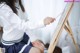 A woman in a school uniform painting on an easel.