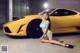 A woman in a blue bikini sitting next to a yellow sports car.