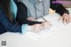 A couple of people sitting at a table with papers and pens.