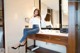 A woman sitting on a vanity in front of a mirror.