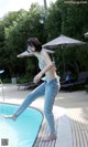 A woman jumping into a swimming pool in a bikini top and jeans.