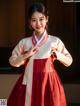 A woman in a red and white hanbok poses for a picture.