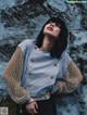 A woman leaning against a stone wall wearing a striped shirt and pearls.